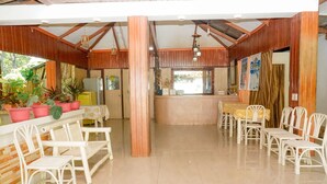 A restaurant with a wooden interior, white chairs, a counter, and potted plants. - Casa Felicisima Inn (Puerto Princesa)