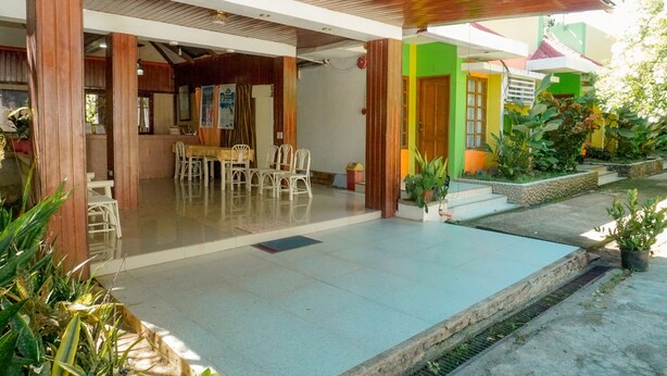 A covered outdoor area with a dining table and chairs, a small garden with potted plants, and a building with colorful walls. - Casa Felicisima Inn (Puerto Princesa)