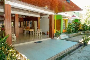 A covered outdoor area with a dining table and chairs, a small garden with potted plants, and a building with colorful walls. - Casa Felicisima Inn (Puerto Princesa)