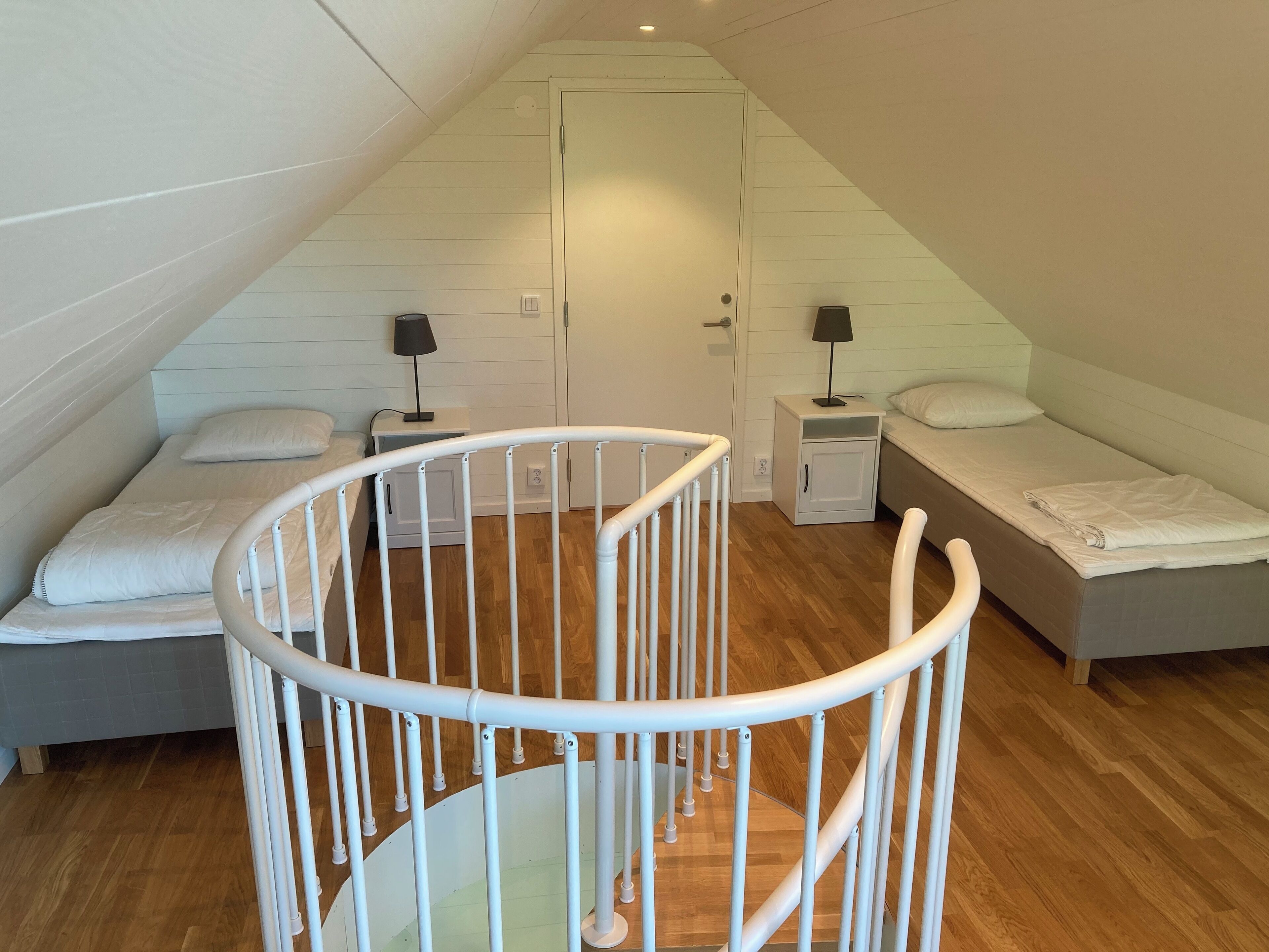 Camera da letto con soffitto spiovente, due letti, una culla bianca e un comodino bianco con una lampada.