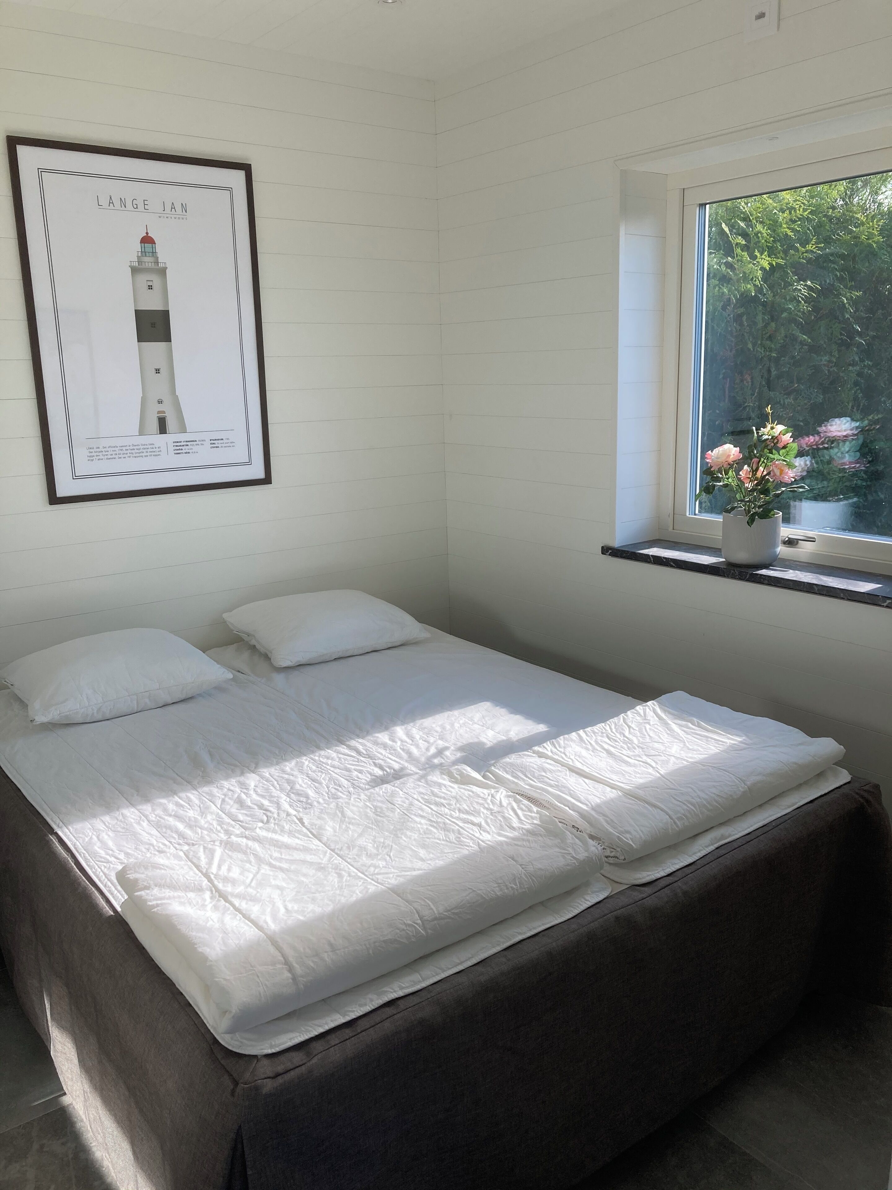 Un dormitorio con cama, ventana con vista a follaje y un cuadro en la pared.