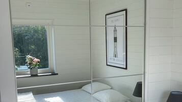 A bedroom with a bed, a nightstand, a lamp, a framed picture on the wall, and a window with a view of greenery.
