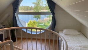 A bedroom with a circular window, a bed, and a white railing. - Brygghuset (Rockneby)