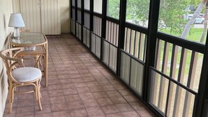 Een balkon met een plafondventilator, een tafel met stoelen en grote ramen met uitzicht op de omgeving.