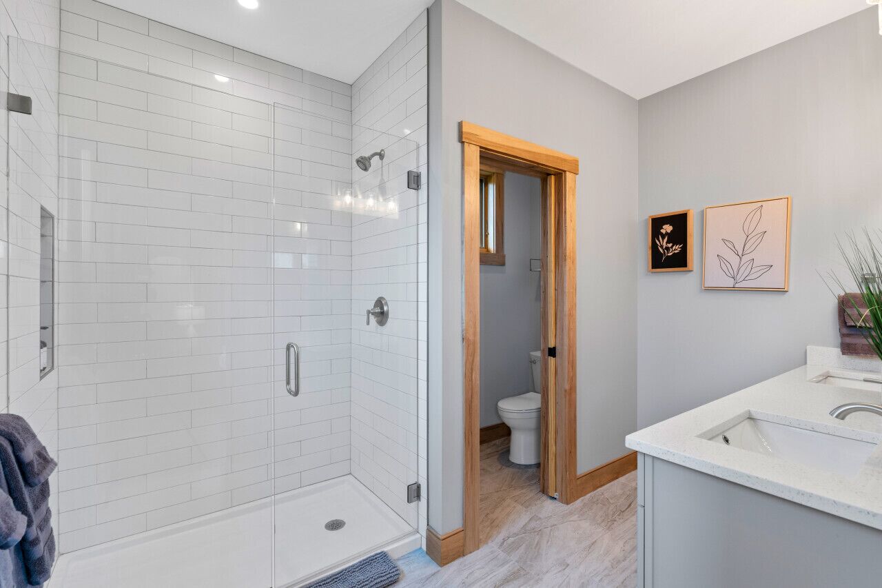 Een moderne badkamer met witte metro tegels, een glazen douchecabine, een houten deur naar een toilet en een wastafel met een spiegel.