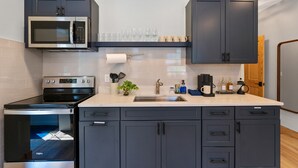 Une cuisine moderne avec des meubles de couleur sombre, un four à micro-ondes, une cuisinière et une machine à café.
