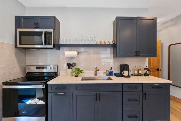A modern kitchen with dark cabinets, a microwave, a stove, and a coffee maker.