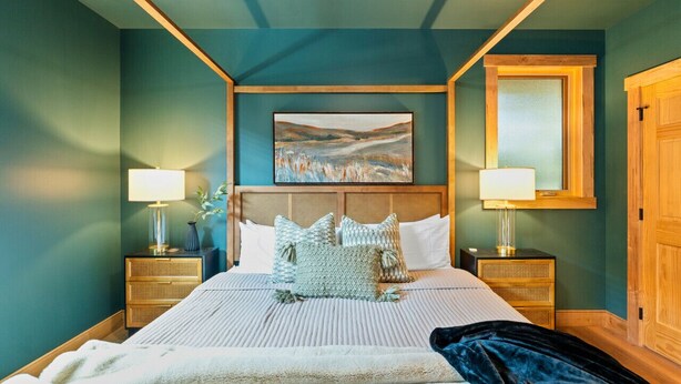 Une chambre à coucher avec un grand lit, deux tables de chevet avec des lampes, une tête de lit et un tableau au mur.