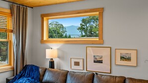 Una habitación con un sofá de cuero, una ventana con vistas a árboles y montañas, y cuadros enmarcados en la pared.