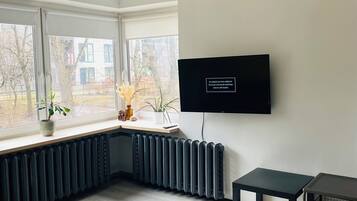 A modern living room with a large window, a radiator, a black table, and a mounted TV.