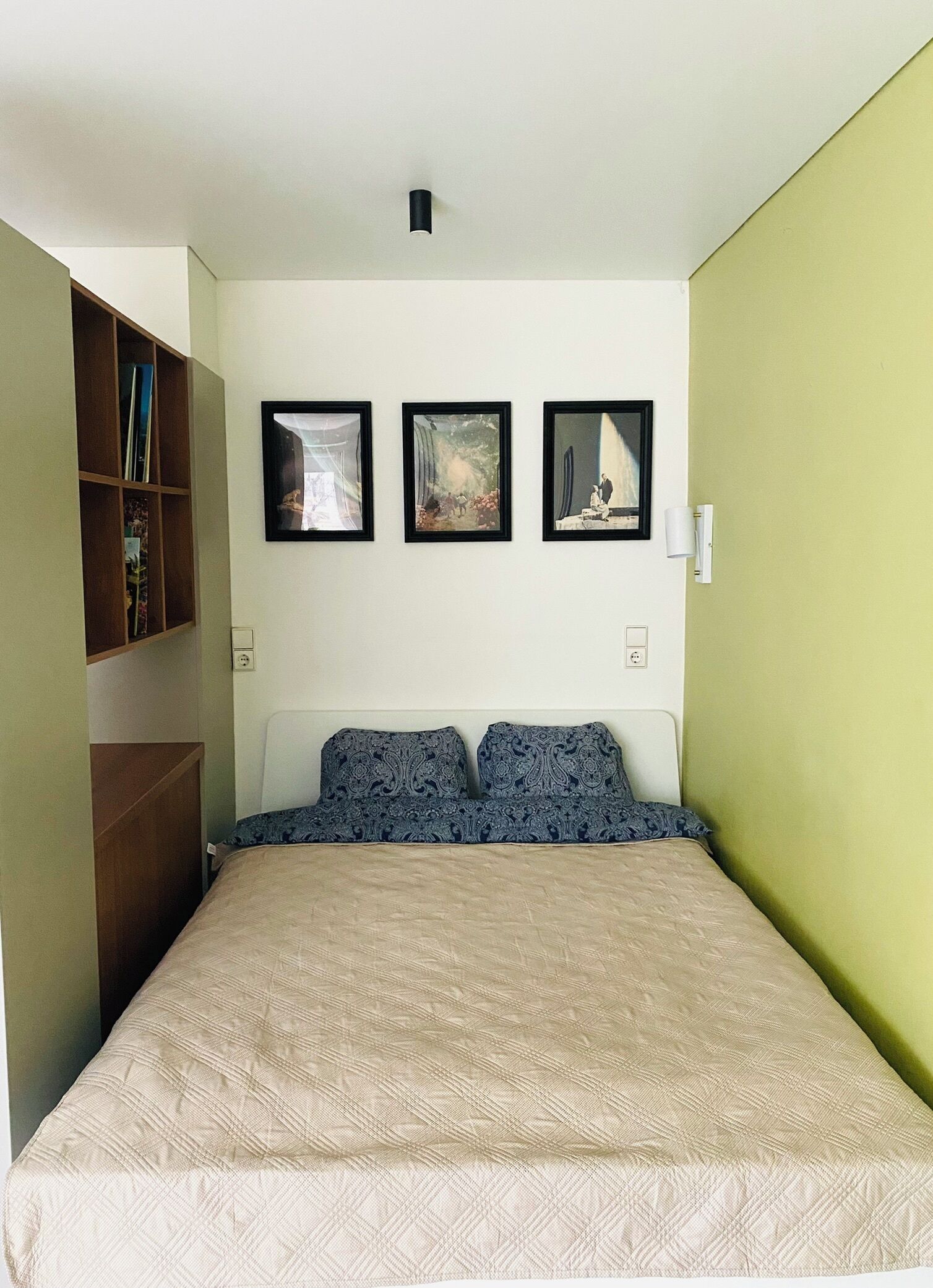 A bedroom with a bed, a bookshelf, and three framed pictures on the wall.