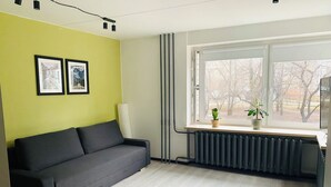 Een moderne woonkamer met een grijze bank, een raam met uitzicht op bomen en een radiator.