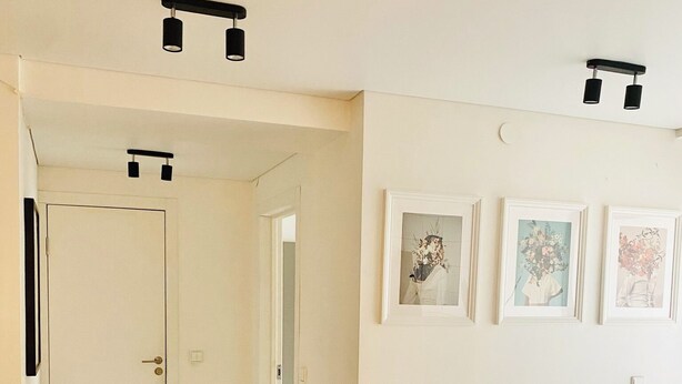Een gang met een deur, een lamp en drie ingelijste foto's aan de muur.