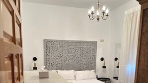 A bedroom with a bed, a nightstand, a dresser, a chandelier, and a decorative headboard. - Casa Rural Cortijo Paulenca  (Almería)