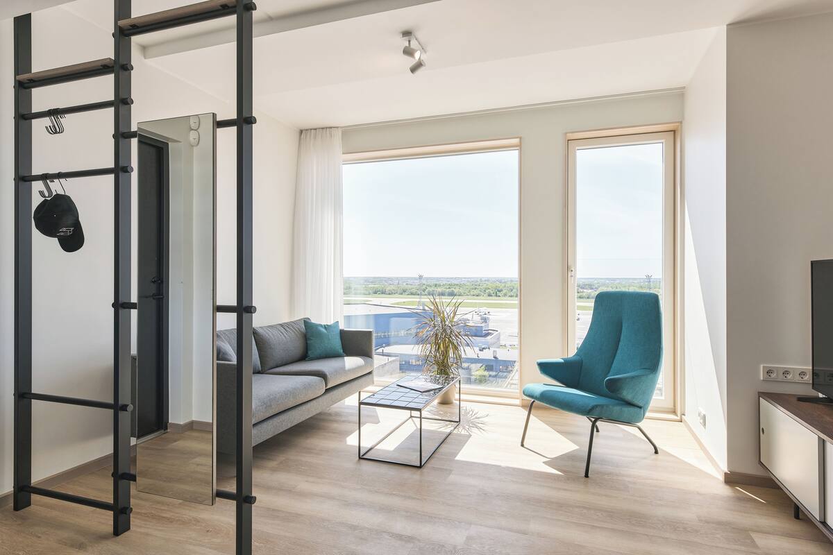 Un salon moderne comprenant un canapé, une table basse, un fauteuil bleu, un meuble pour la télévision et une grande fenêtre donnant sur la ville.