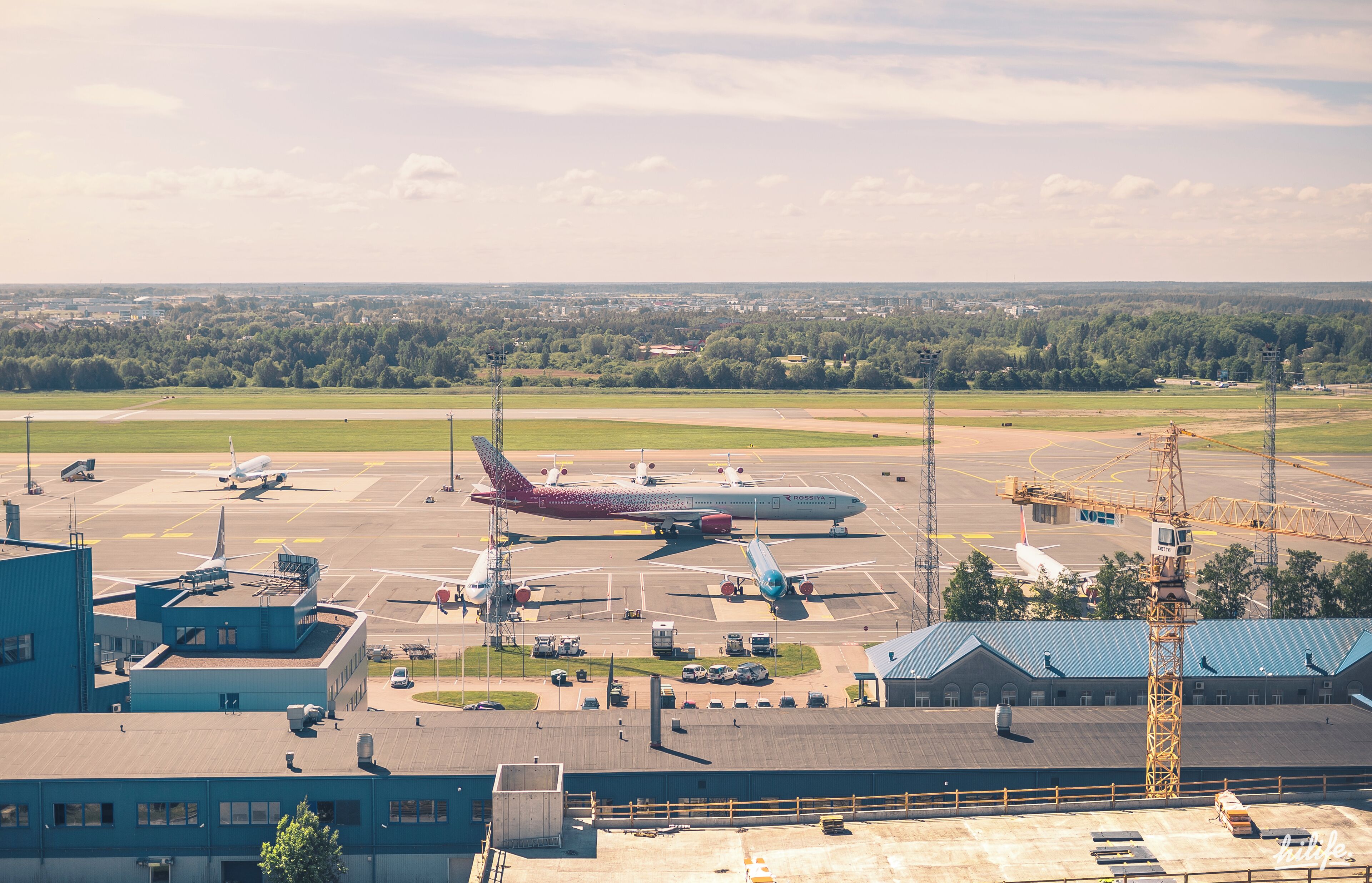 An airport tarmac with multiple airplanes, airport buildings, and a distant cityscape.