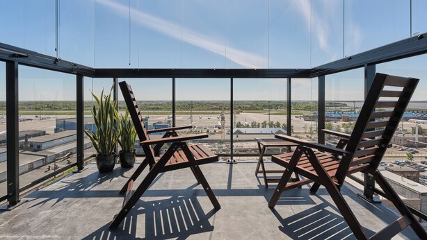 A glass-enclosed balcony with two wooden chairs and a table, overlooking an airport and distant landscape. - LURICH Residences (Tallinn)
