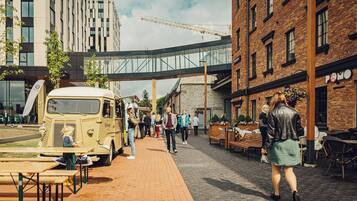 A street with a vintage food truck, outdoor seating, and a pedestrian bridge.