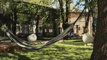 A hammock tied between trees in a grassy area with a stone wall and a building in the background.
