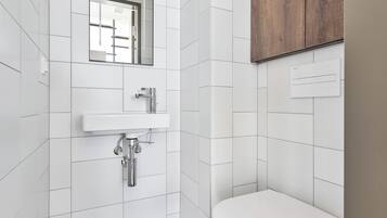 A modern bathroom with white tiles, a white sink, a mirror, and a wooden cabinet.