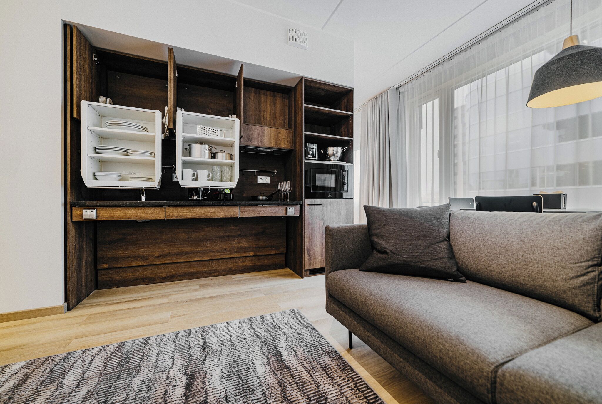A modern living room with a built-in wooden shelving unit, a gray sofa, and a patterned rug.