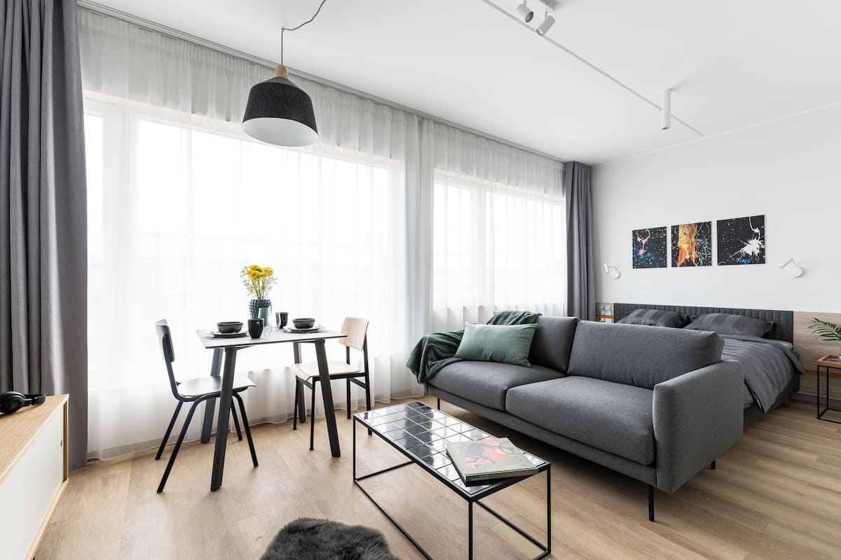 Un salon moderne avec un canapé gris, une table basse en verre, une table à manger avec des chaises et un luminaire suspendu.