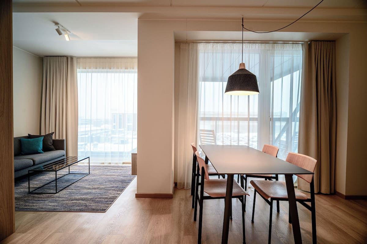 Un salon moderne avec un canapé, une table à manger et une grande fenêtre agrémentée de rideaux.