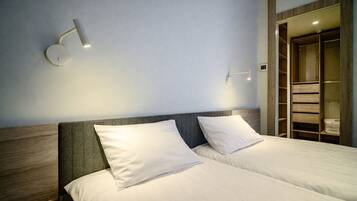 Quarto de hotel com duas camas, cabeceira de madeira e guarda-roupa embutido com prateleiras.