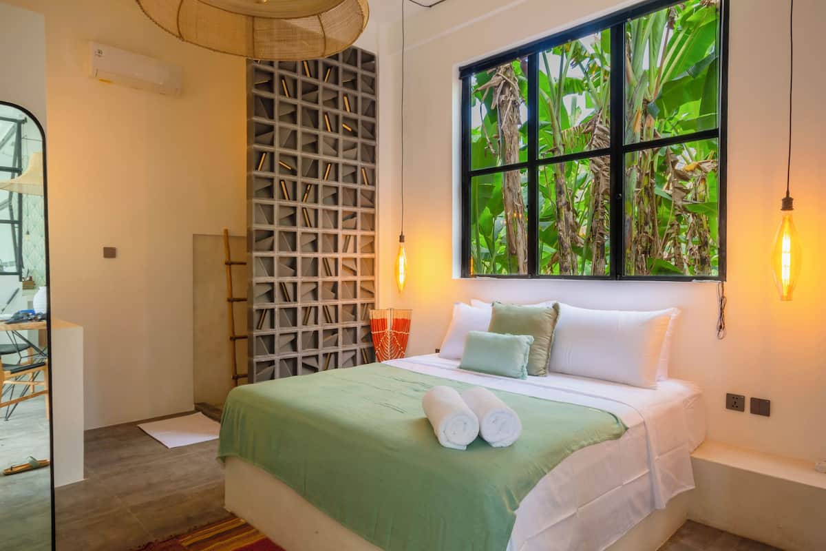 A neatly arranged bedroom with a large window, a bed with white linens, and a wall-mounted shelf.