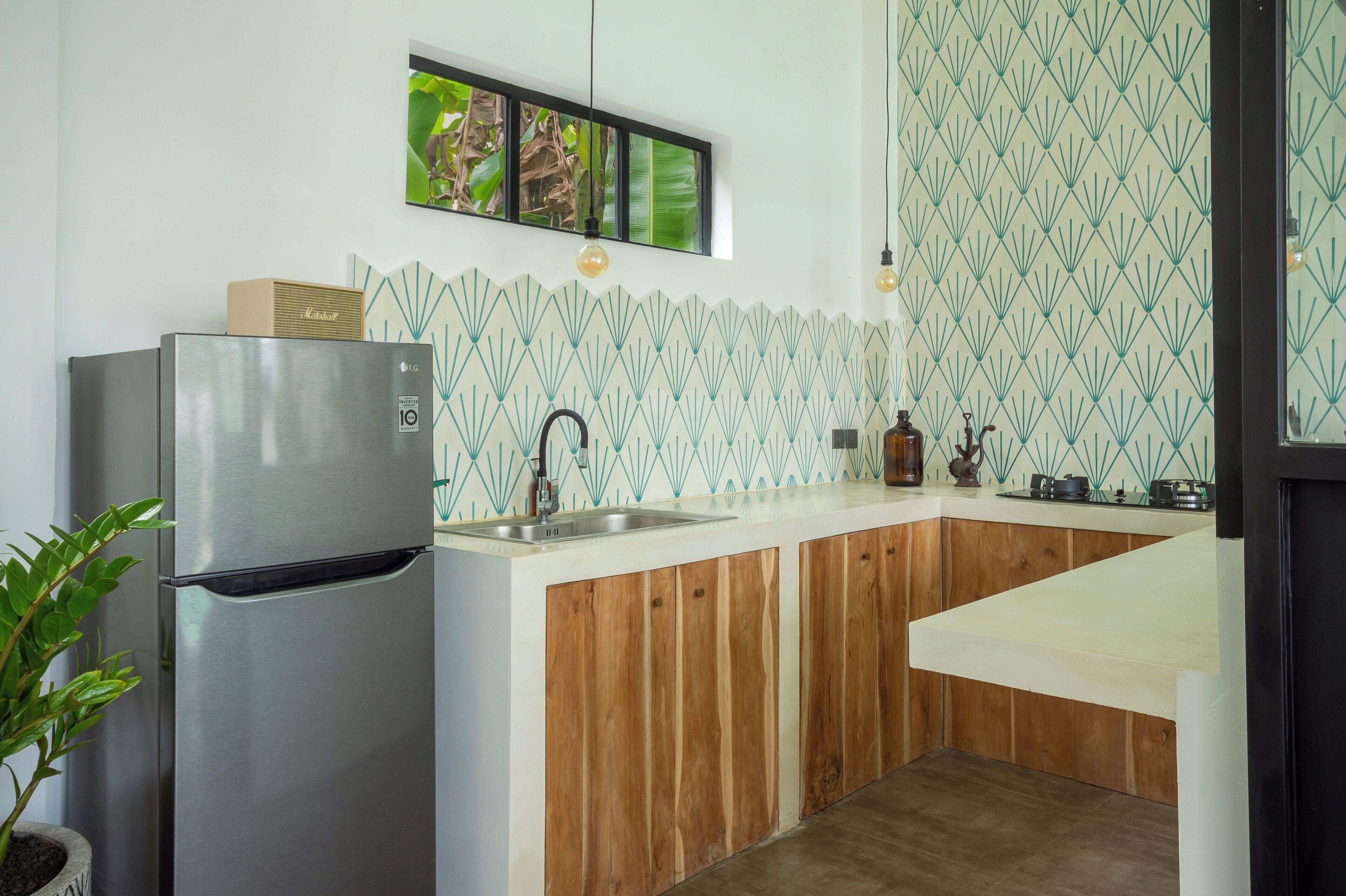 A kitchen with a stainless steel refrigerator, wooden cabinets, a white countertop, and a backsplash with a geometric pattern.