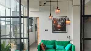 A modern living room with a green sofa, a wooden coffee table, and a colorful rug. There are pendant lights above the sofa and a framed picture on the wall. - MariNara Lofts (Canggu)