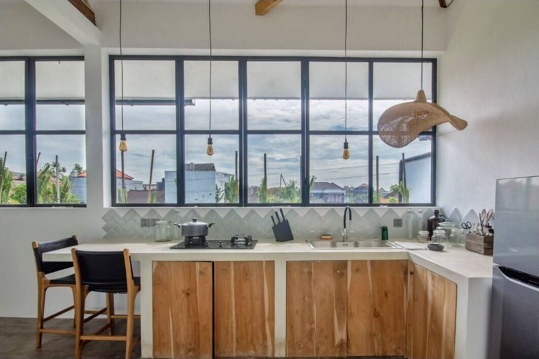 A modern kitchen with large windows, a wooden island, and a view of buildings and greenery.
