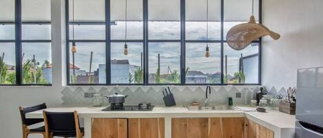 A modern kitchen with large windows, a wooden island, and a view of buildings and greenery.
