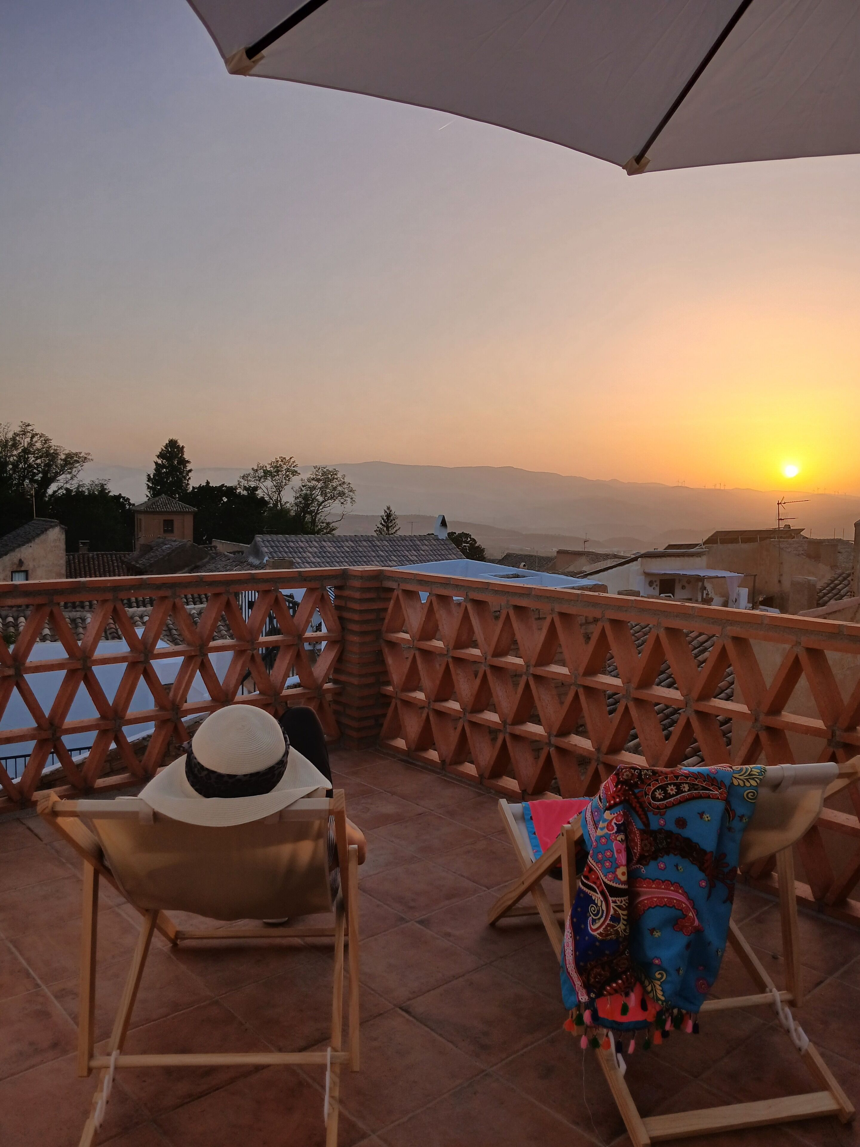 Une terrasse offrant une vue sur le coucher de soleil, des chaises en bois et une table.