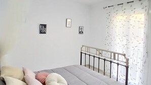 Camera da letto con un letto, cuscini, testiera, una lampada a soffitto e una finestra con tende.