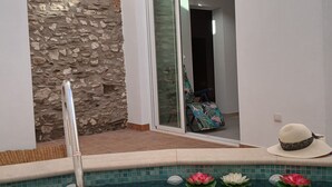 Una piscina con acqua cristallina, un muro in pietra e una porta scorrevole in vetro che conduce a una stanza.