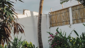 A white building with a bamboo fence, surrounded by lush greenery and a palm tree. - Ningaloo Villa (Gili Trawangan)