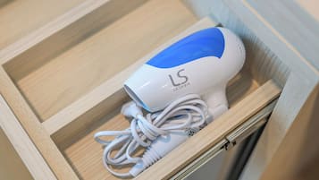A white and blue hair dryer with a cord, placed inside a wooden drawer.