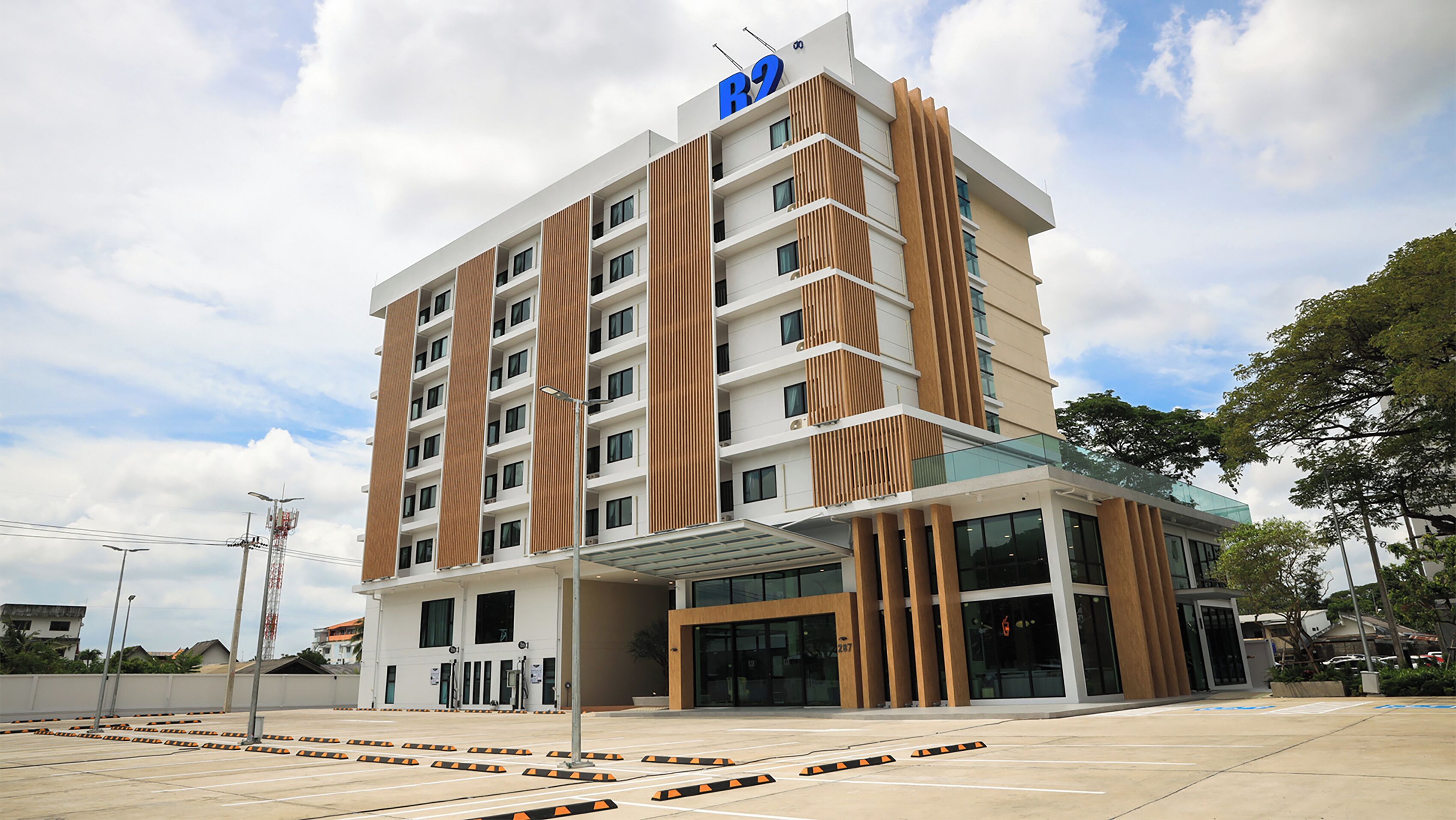 A modern multi-story hotel with a prominent 'R2' sign, a glass entrance, and a parking lot with marked spaces.
