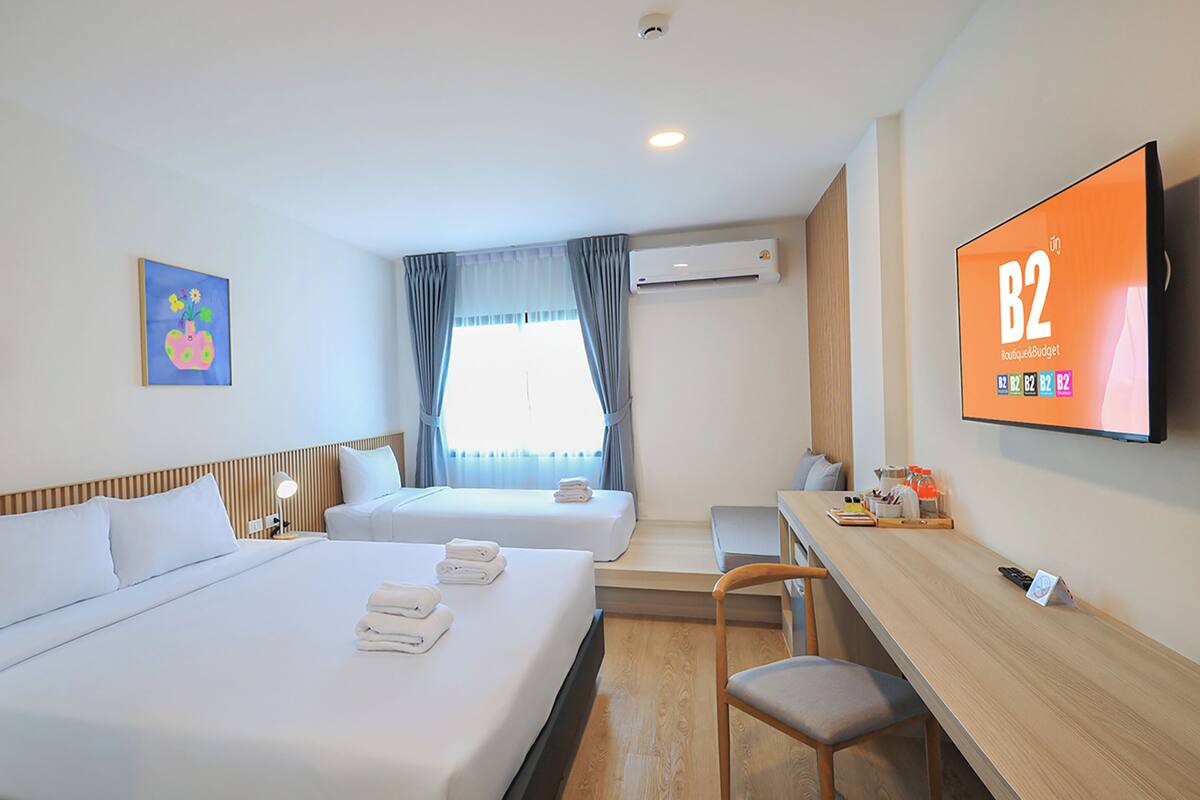 A hotel room with two beds, a desk, a chair, a TV, and artwork on the walls.