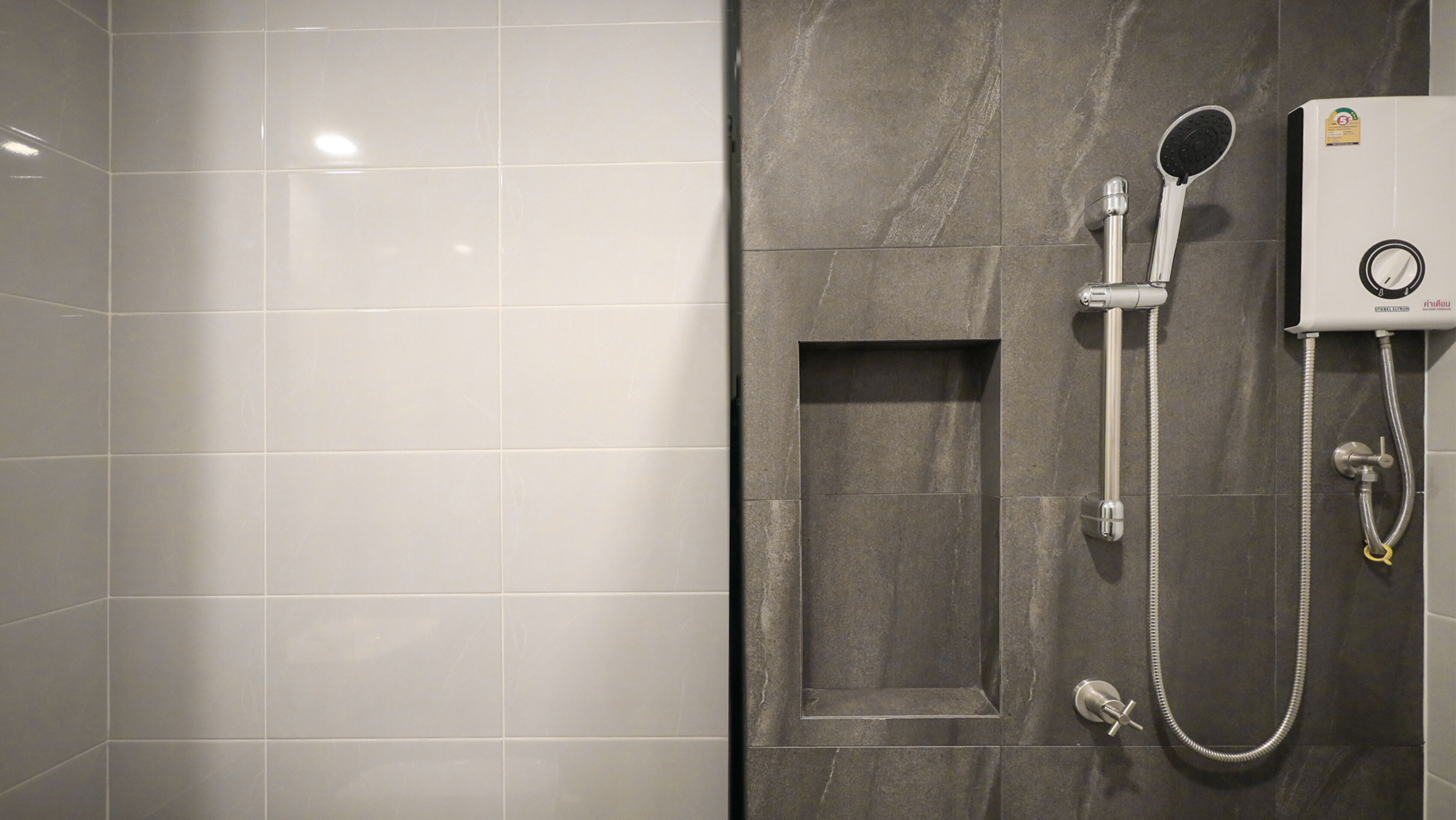 A bathroom with white tiles, a dark marble wall, and a shower unit with a handheld showerhead and hose.