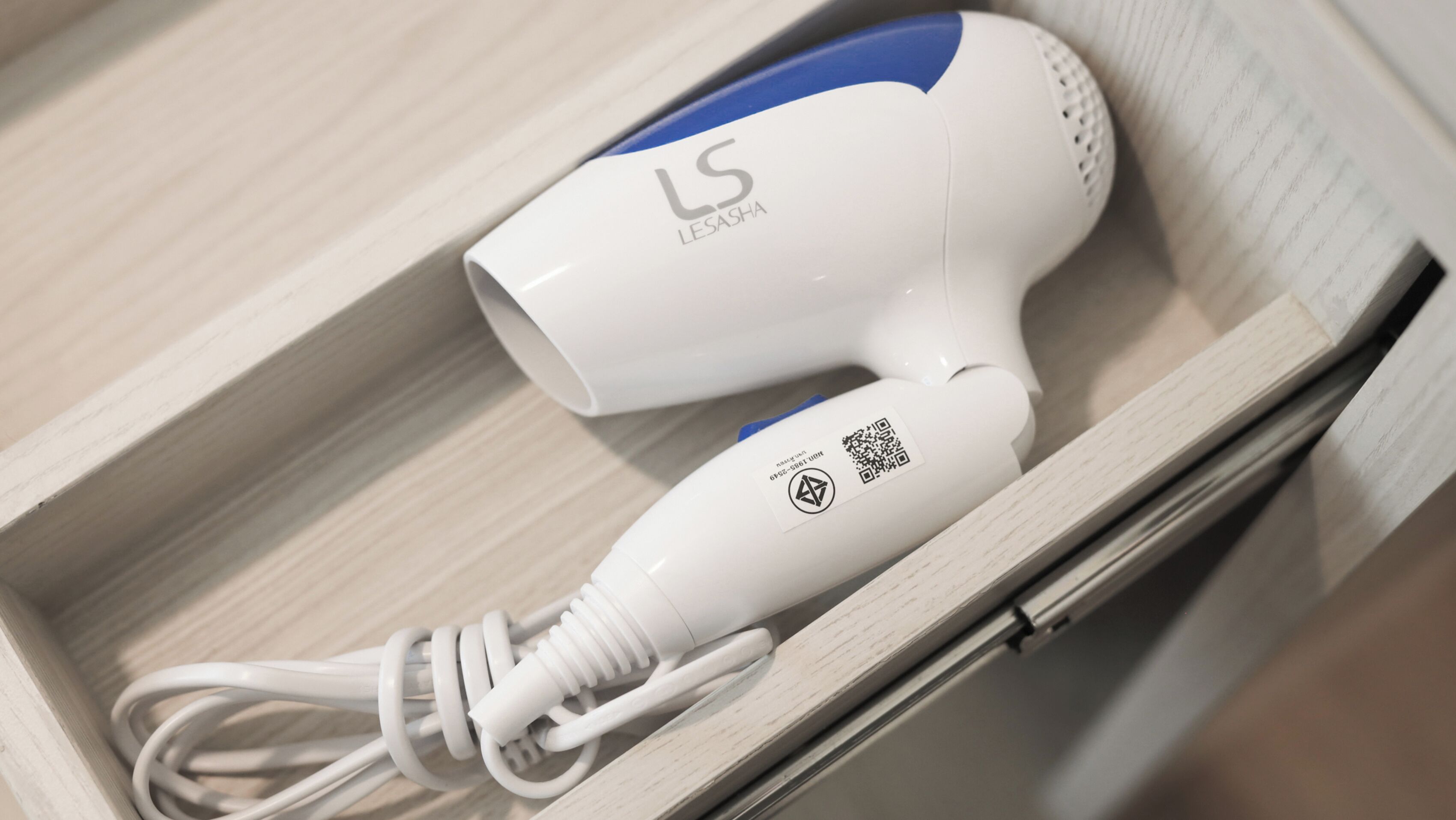 A white and blue hair dryer with a cord, placed in a wooden box.