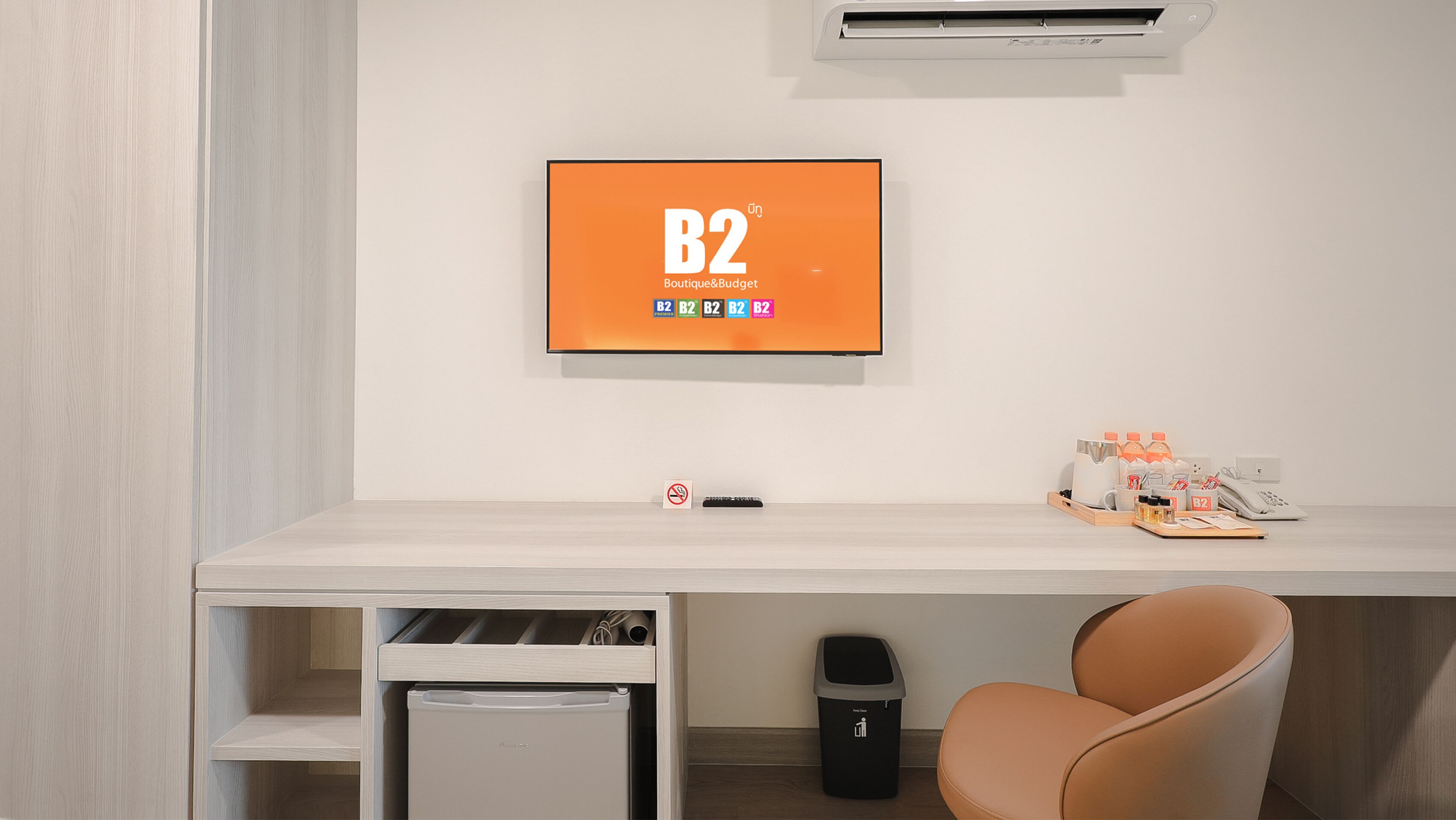 Un espace de bureau moderne comprenant un bureau, une chaise et un écran fixé au mur affichant le texte « B2 Boutique&Budget ».