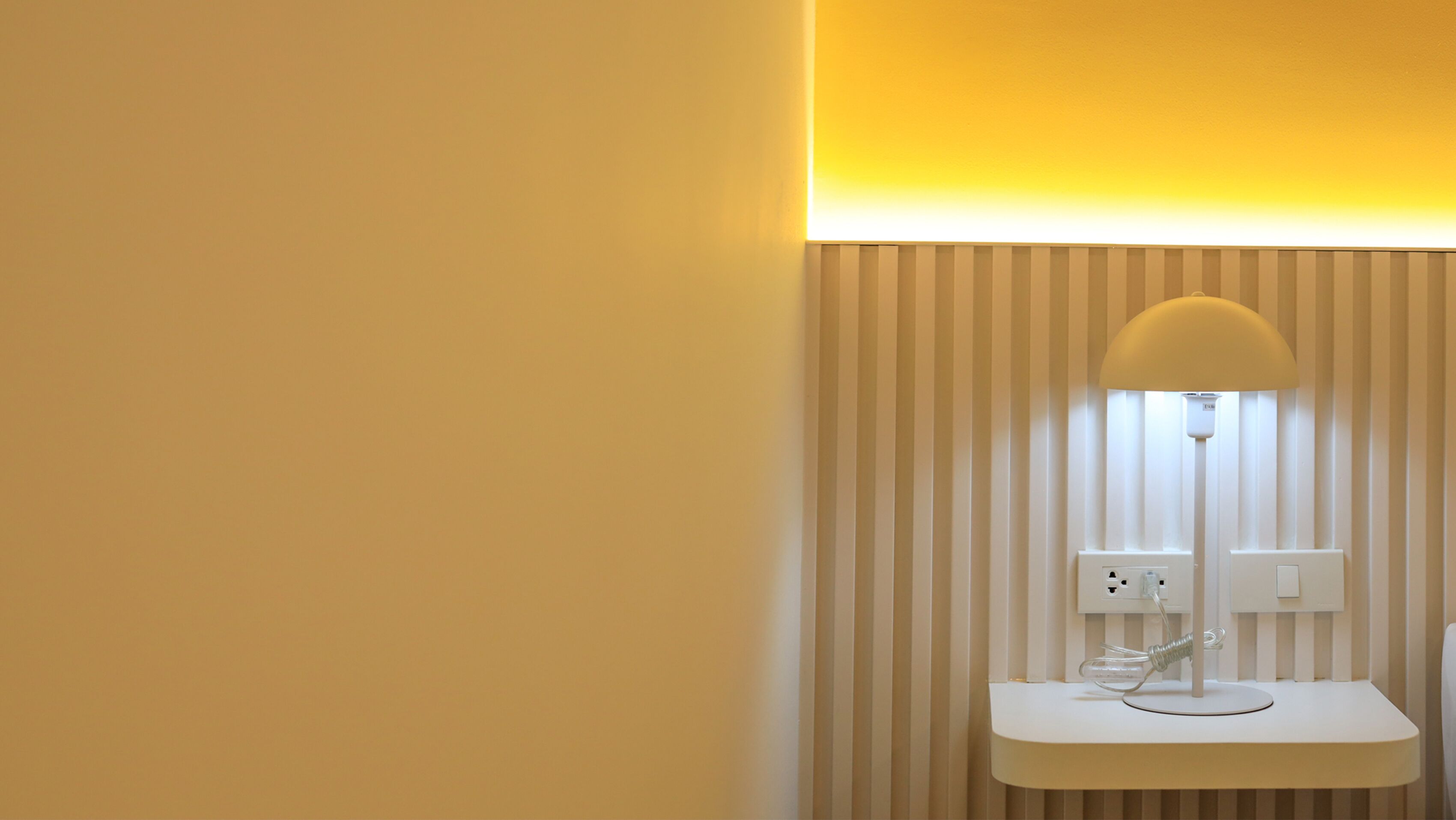 A modern room with a white bedside table, a lamp, and a power outlet.