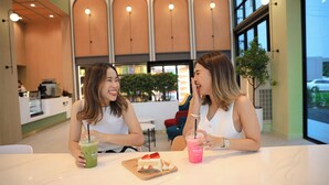 Two people sitting at a table with drinks and a dessert in a modern cafe with large windows and a view of the street outside. - B2 Ubon Airport Premier Hotel (Ubon Ratchathani)