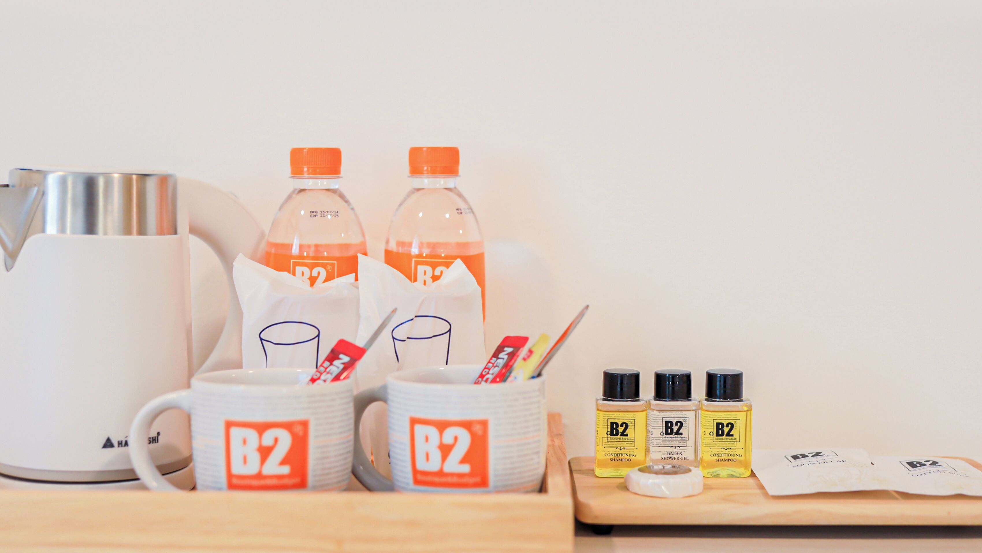 A kitchen setup with a kettle, two B2 branded bottles, a mug, a tissue, and B2 shampoo bottles.