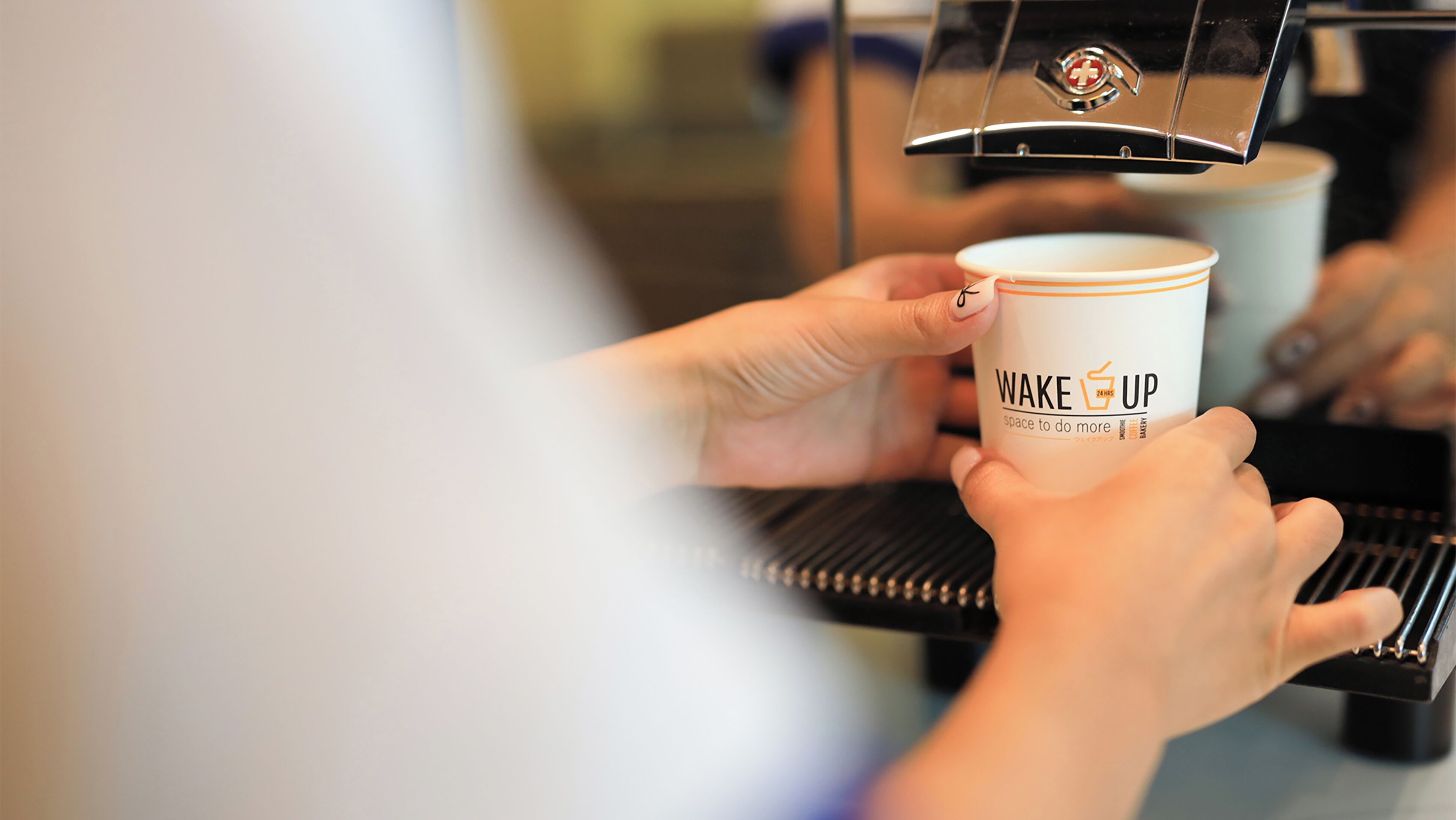 A person holding a coffee cup with the text "WAKE UP" and "space to do more" on it.