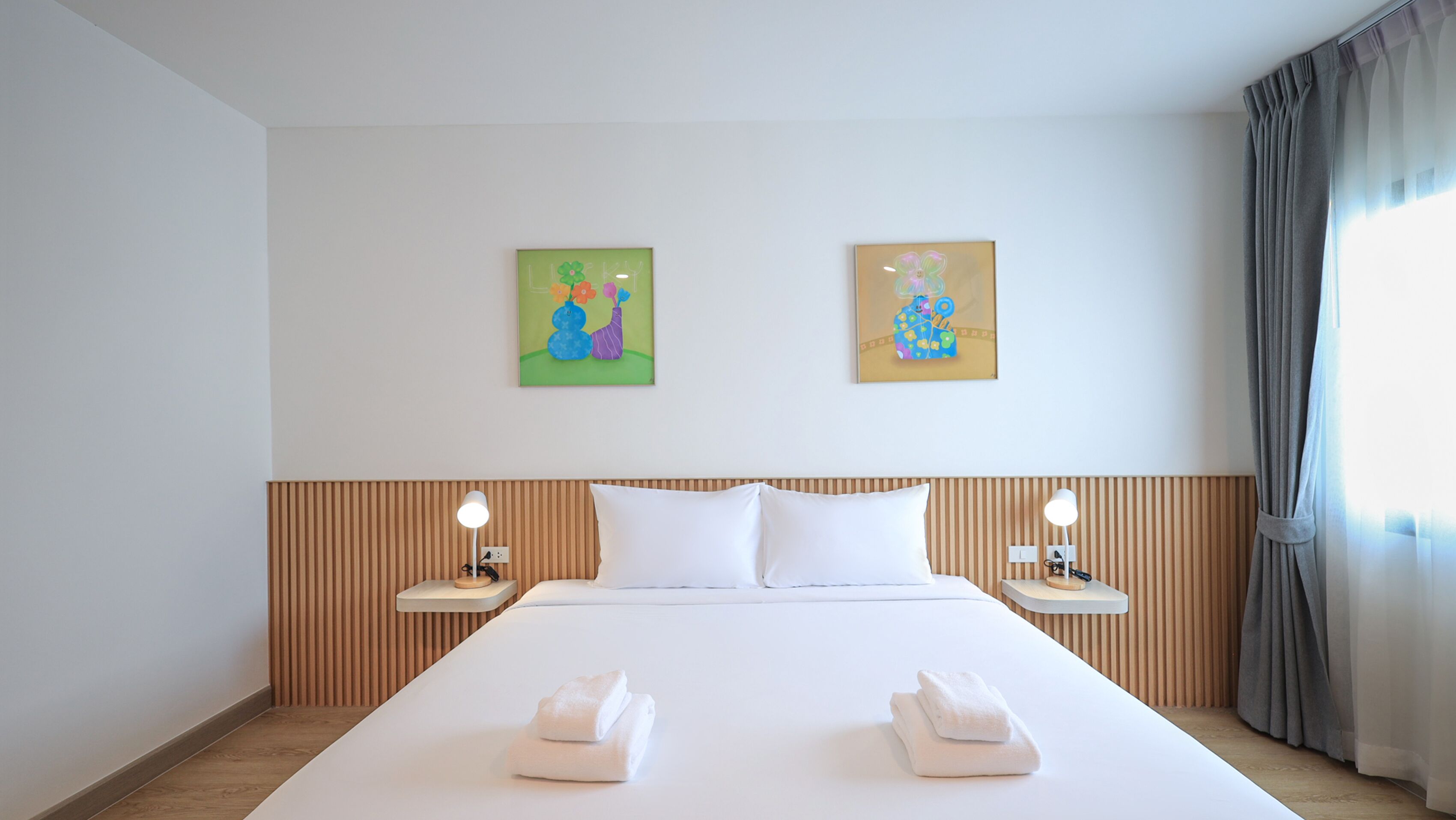 A hotel room with a large bed, two pillows, two bedside tables with lamps, and two wall-mounted paintings.