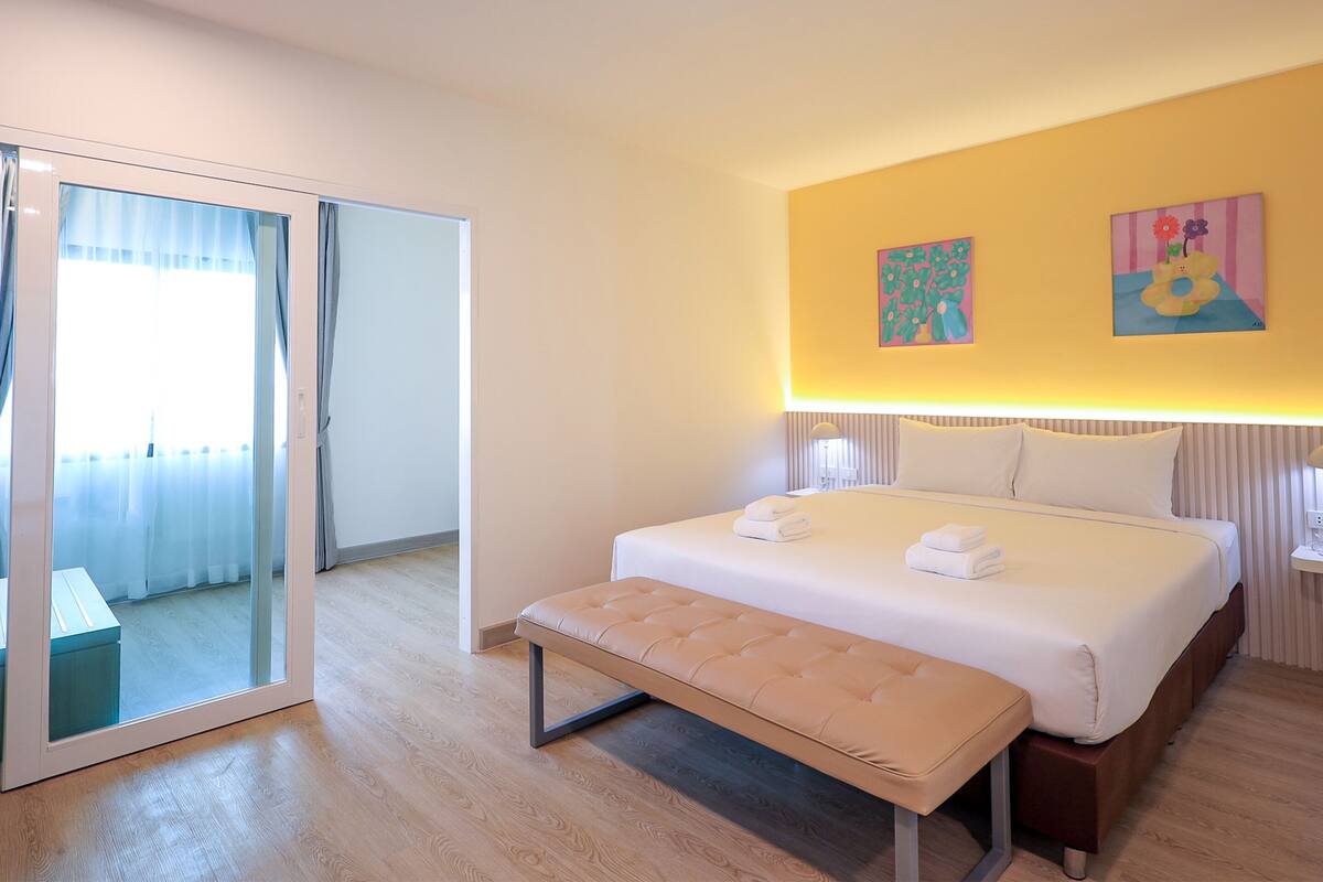 A hotel room with a bed, bench, and two paintings on the wall.