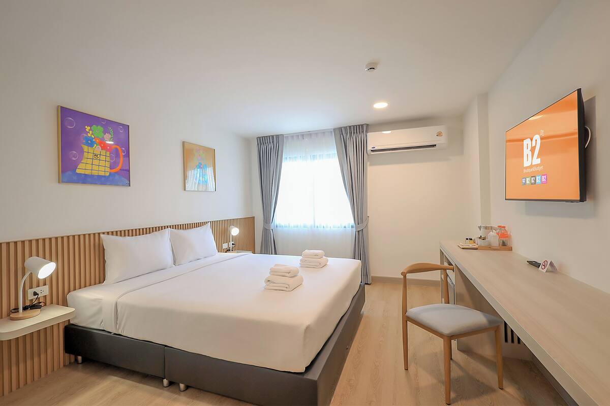 A hotel room with a bed, a desk, a chair, a TV, and artwork on the walls.